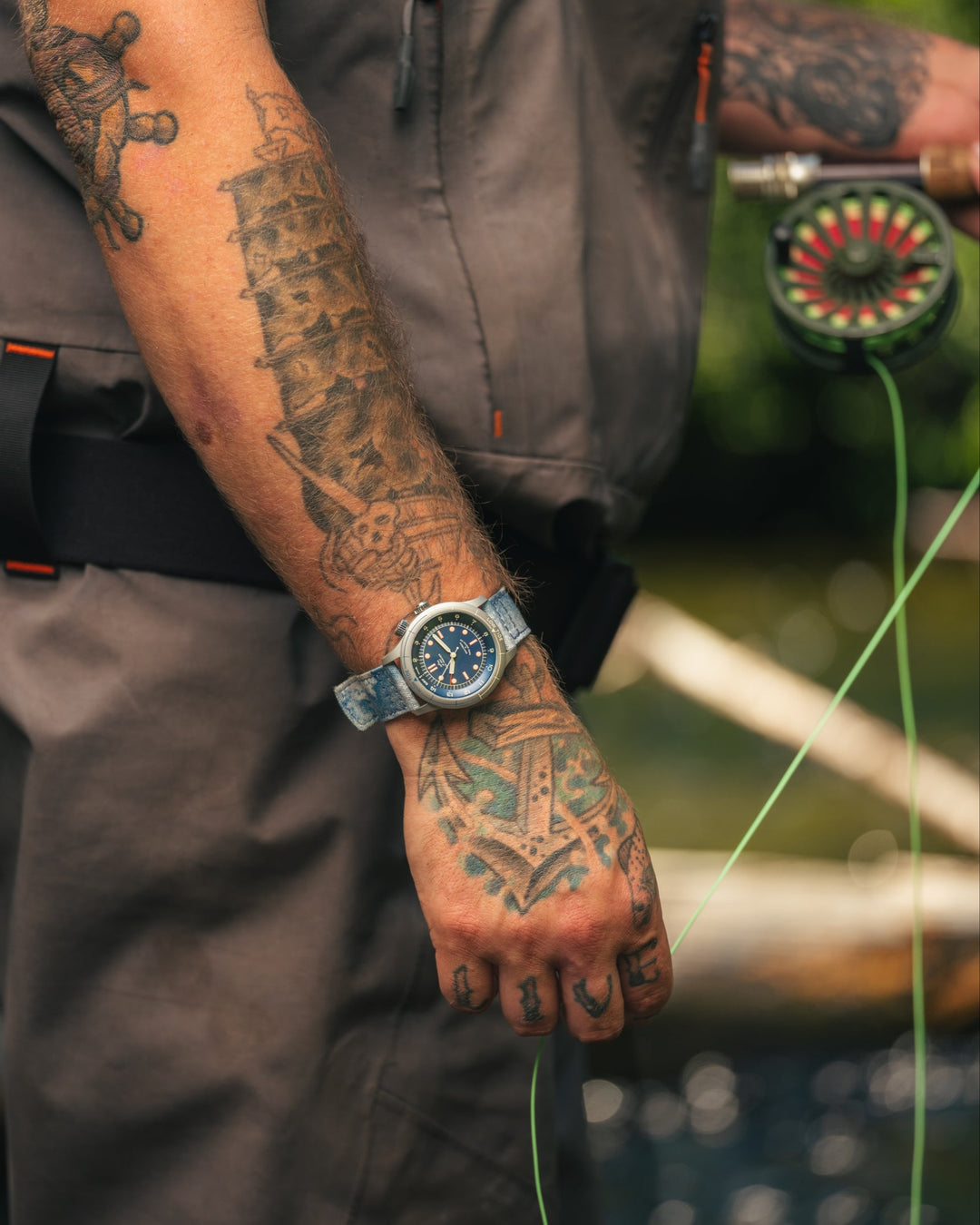Person wearing a watch with tattoos on their arm, holding fishing equipment.