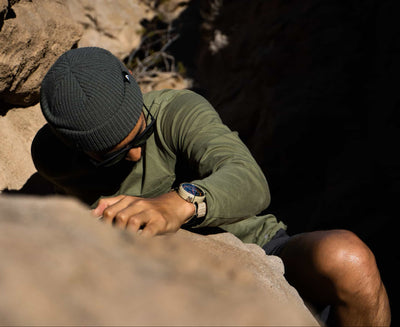 Person climbing a rock face wearing a green shirt and black beanie.